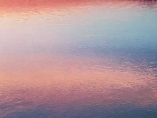 The image shows a serene body of water with a gradient of colors reflecting the sky above. The water is a light blue color at the top and gradually transitions into a darker shade towards the bottom. The reflection on the water's surface creates a beautiful pattern that adds depth to the scene.
