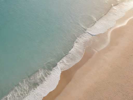 The image shows an aerial view of a beach scene with light brown sand and turquoise water. The shoreline is visible on the right side of the photo, where white waves are crashing onto the sandy beach.