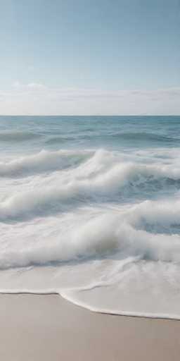 The image shows a serene beach scene with a large body of water and the ocean extending into the distance. The sky above is clear blue with some clouds scattered across it. On the left side of the photo, there's a gray wall that contrasts with the natural elements on the right side.