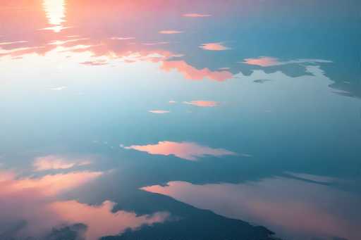 A stunning photograph captures a serene sky at either sunrise or sunset, with the sun positioned in the upper left corner. The sun's rays cast a warm, pinkish-orange glow across the scene, illuminating the clouds and creating a mesmerizing interplay of colors. The sky is predominantly blue, with a gradient that transitions from a lighter blue near the horizon to a deeper blue at the top. The clouds, which are scattered throughout the sky, are tinged with pink and orange hues, adding to the ethereal beauty of the image. The overall composition is simple yet captivating, focusing solely on the sky and its magnificent colors.