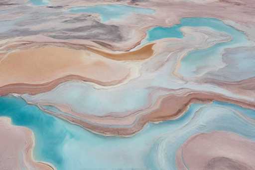 The image shows an aerial view of a large body of water with a unique pattern resembling the scales of a fish or the ripples on the surface of a pond. The colors used in the image are predominantly blue and pink, creating a visually striking contrast against the brownish-orange hues of the surrounding landscape.