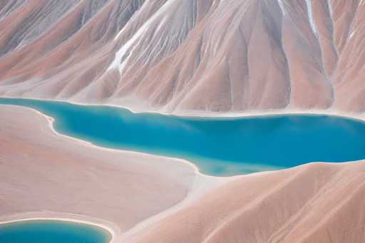 The image showcases a breathtaking aerial view of a vibrant turquoise lake nestled amidst stark, reddish-brown mountains. The water's surface is strikingly smooth, reflecting the surrounding landscape. The mountains exhibit a textured, almost sculpted appearance with subtle variations in color and tone, suggesting erosion. The overall style is a serene, almost otherworldly landscape photograph emphasizing the vastness and tranquility of nature.